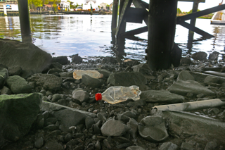 plastic water bottles underneath a bridge near the water.